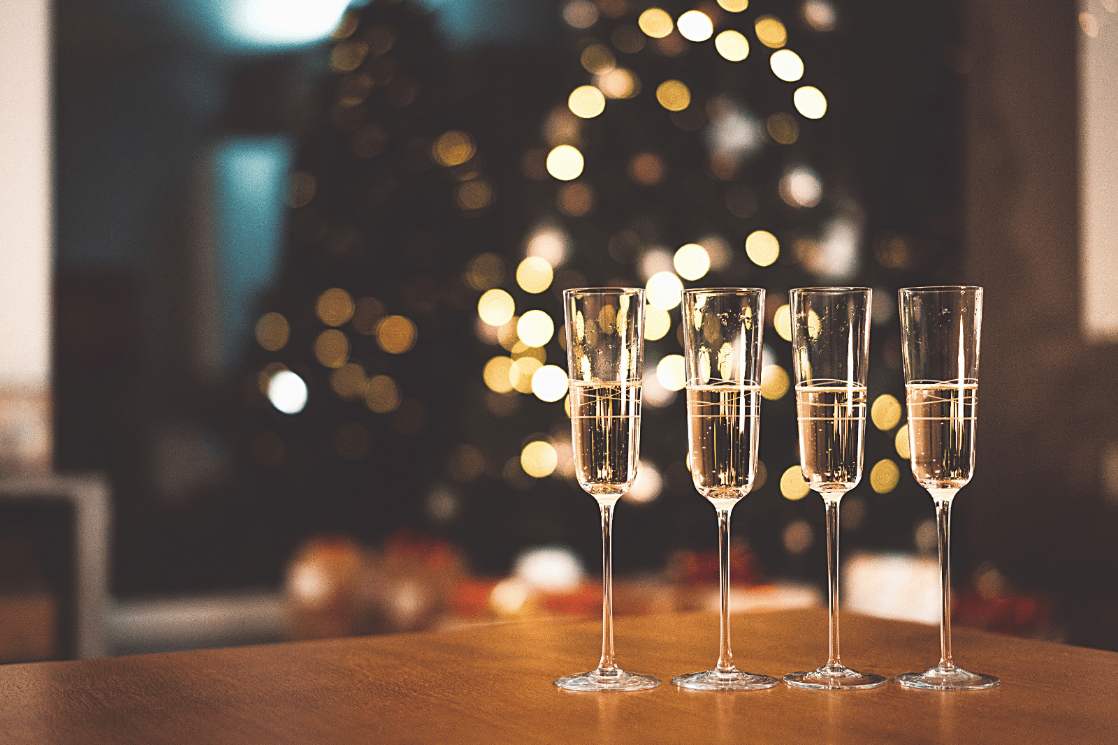 Image featuring four elegant champagne glasses near a decorated Christmas tree
