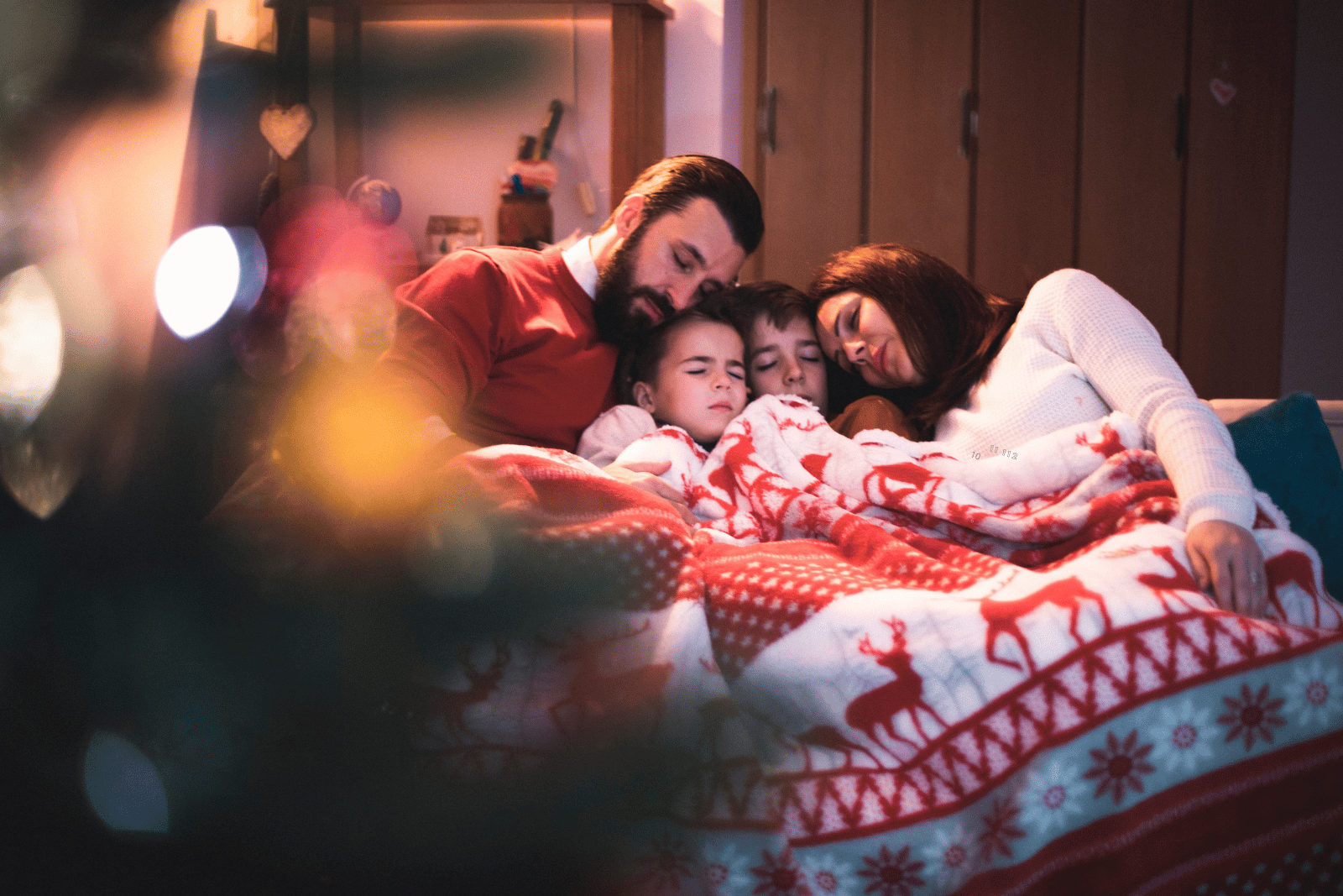 Image featuring a family snuggled up on a bed, surrounded by twinkling Christmas lights